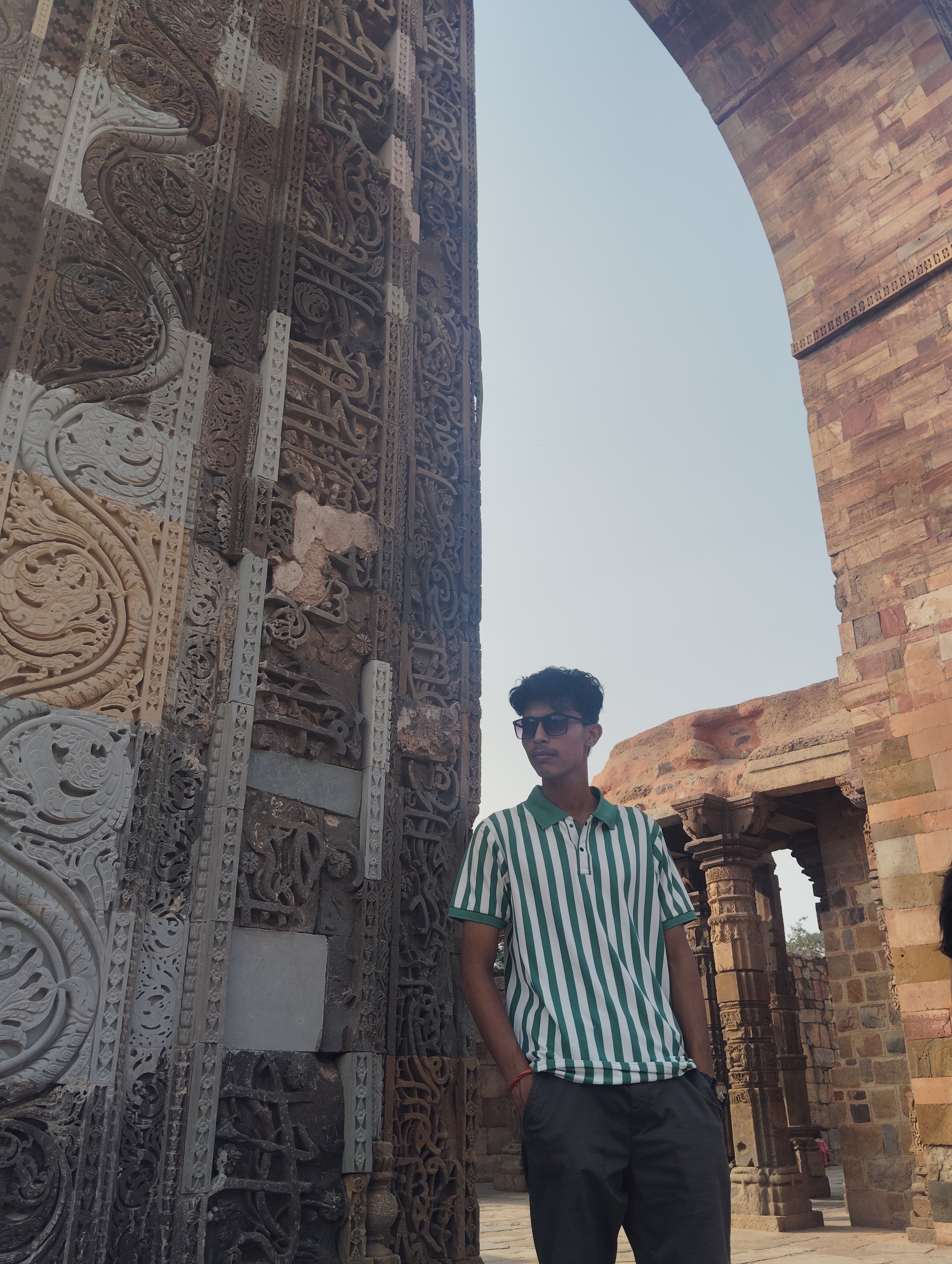 Ashish Alam Kabir beside detailed historic stone carvings at the Qutub complex