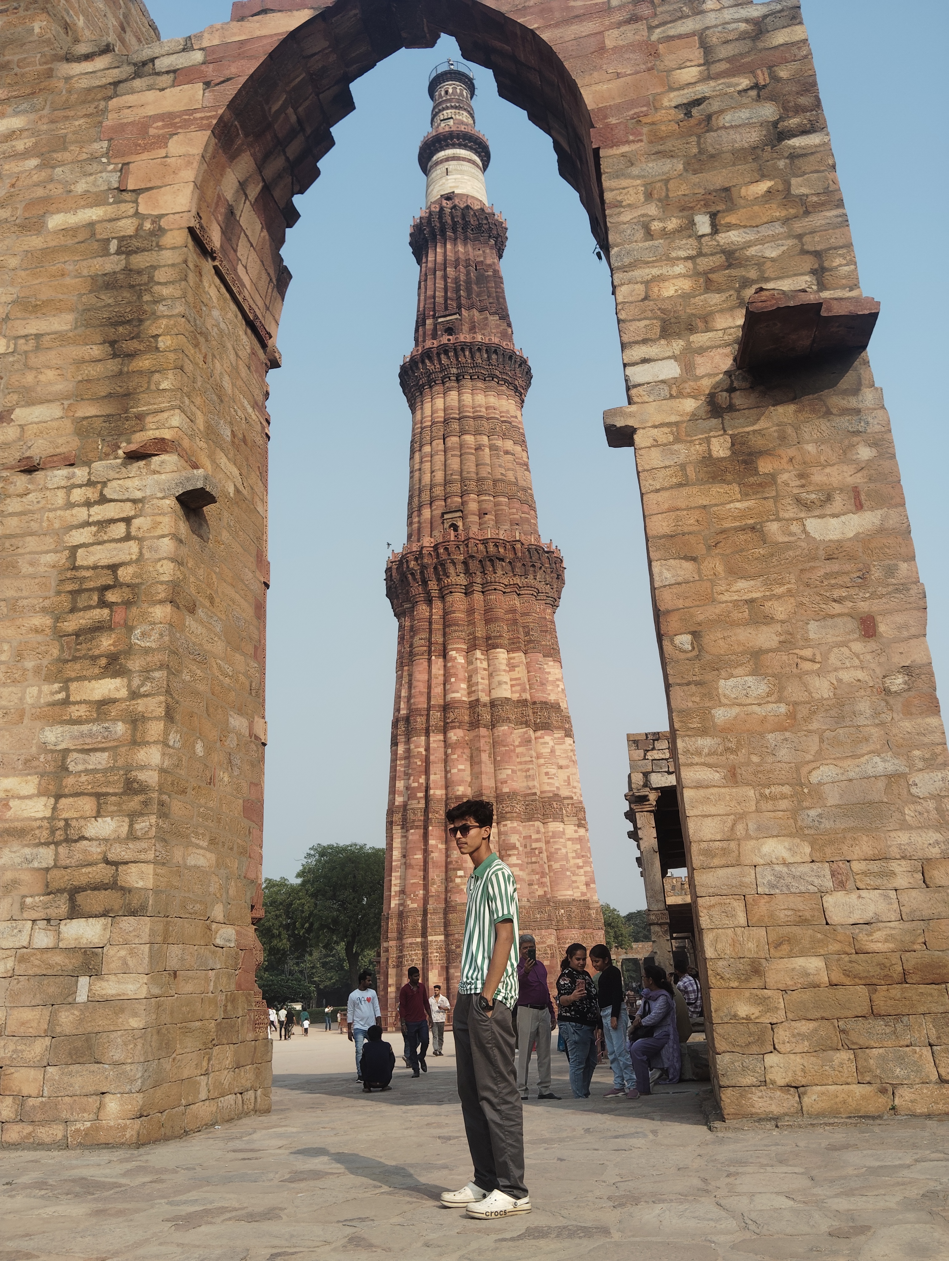 Ashish Alam Kabir standing beneath a stone arch with Qutub Minar behind him