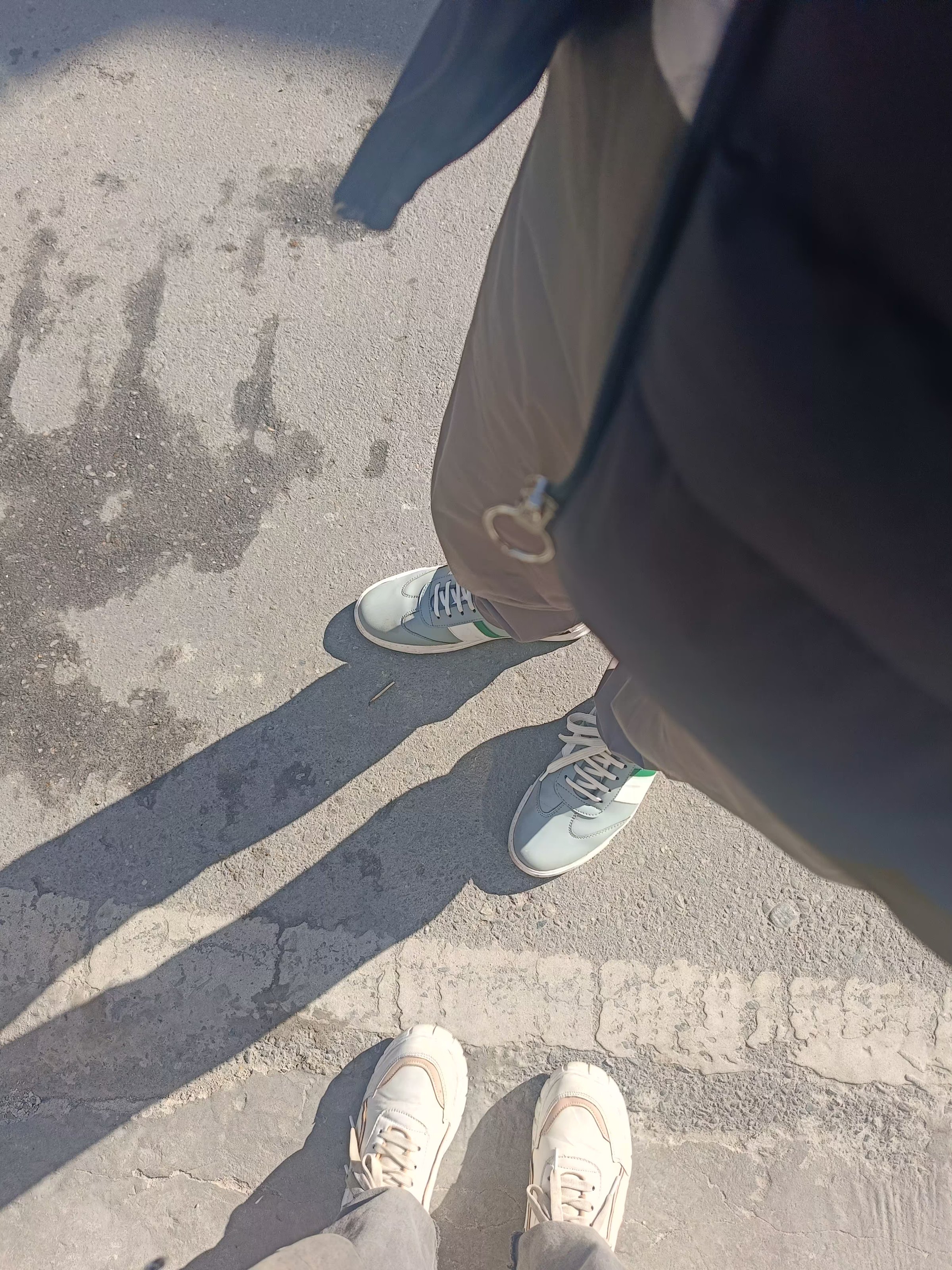 Two pairs of shoes and their shadows on a sunlit mountain road