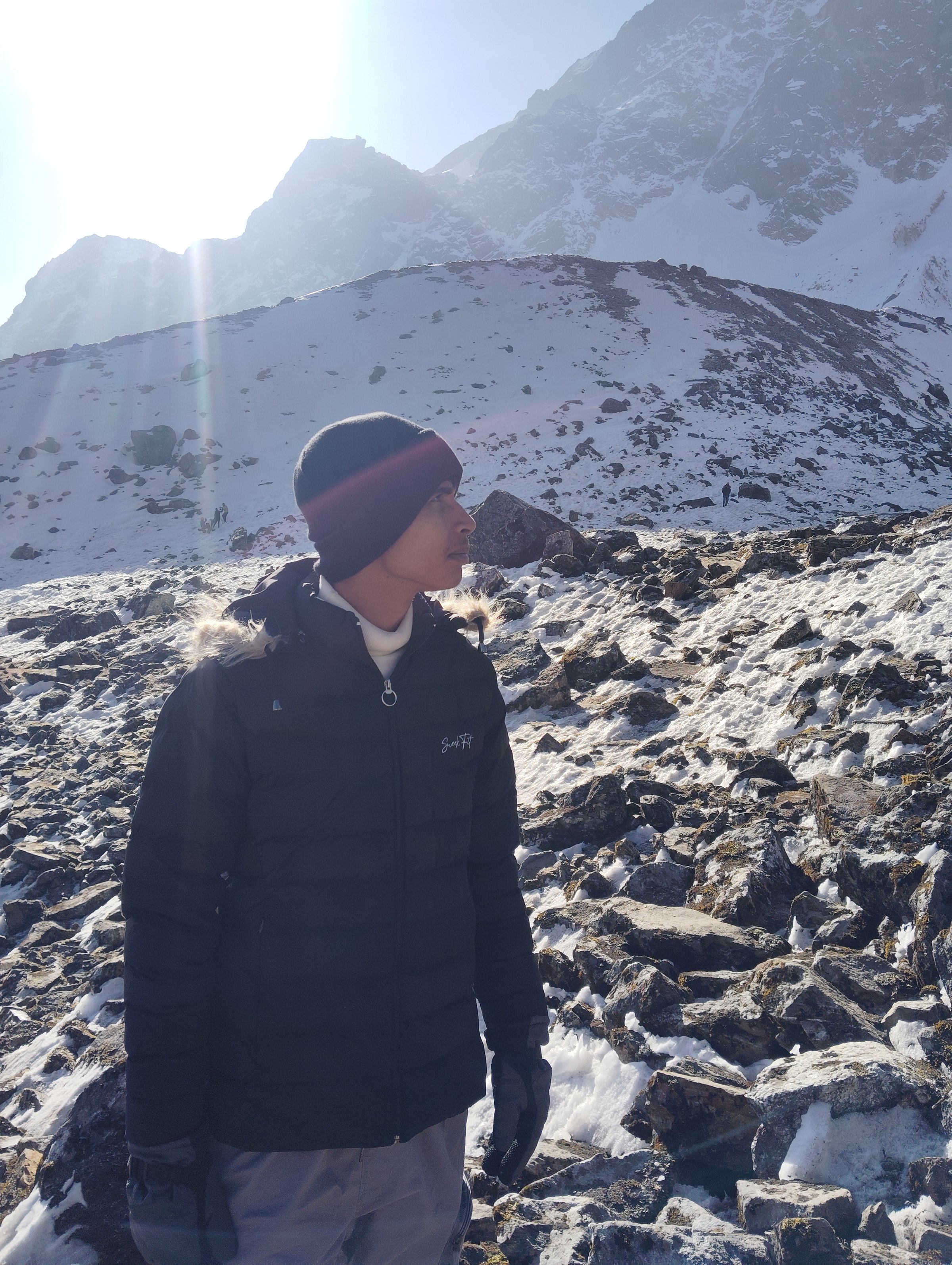Ashish Alam Kabir standing among snowy rocks beneath high mountain peaks