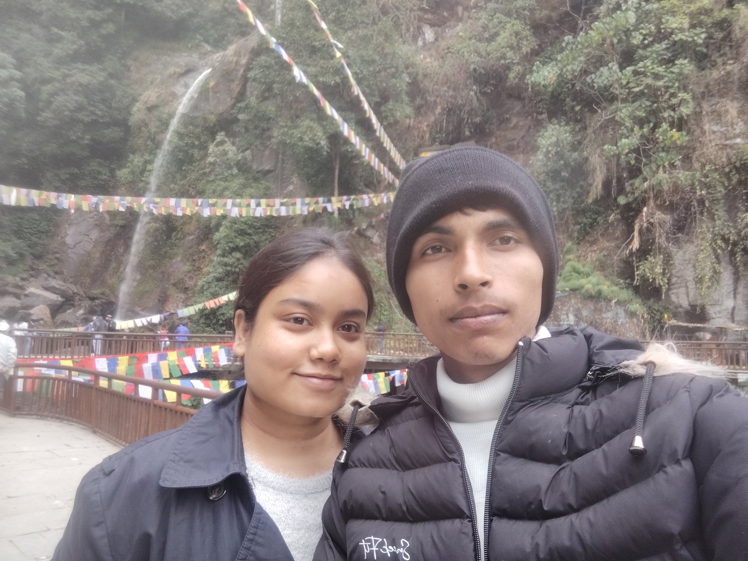Ashish Alam Kabir and a companion taking a selfie near a waterfall and prayer flags